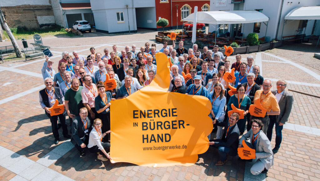 Gruppenfoto von Energie in Bürgerhand. Die vordere Reihe hält einen großen Banner in Form eines Daumen nach oben.