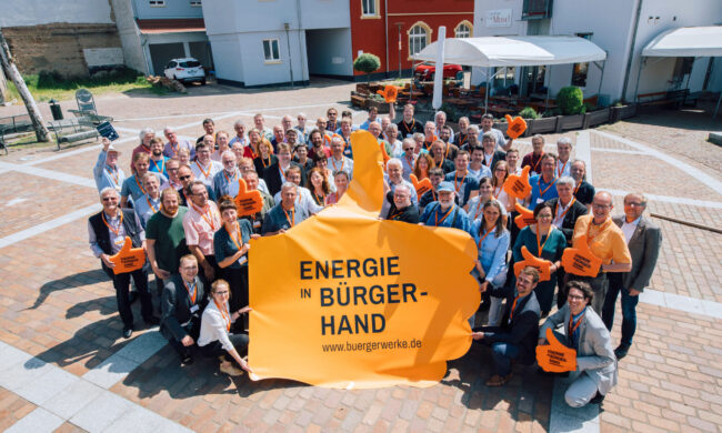Gruppenfoto von Energie in Bürgerhand. Die vordere Reihe hält einen großen Banner in Form eines Daumen nach oben.