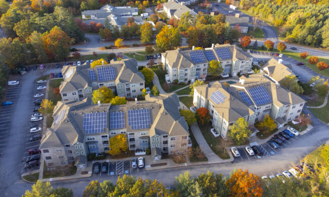 Luftaufnahme von Mehrfamilienhäusern mit auf dem Dach installierten Solarzellen im Herbst